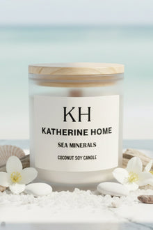 Candle labeled 'KH Katherine Home' with sea minerals on a beach setting