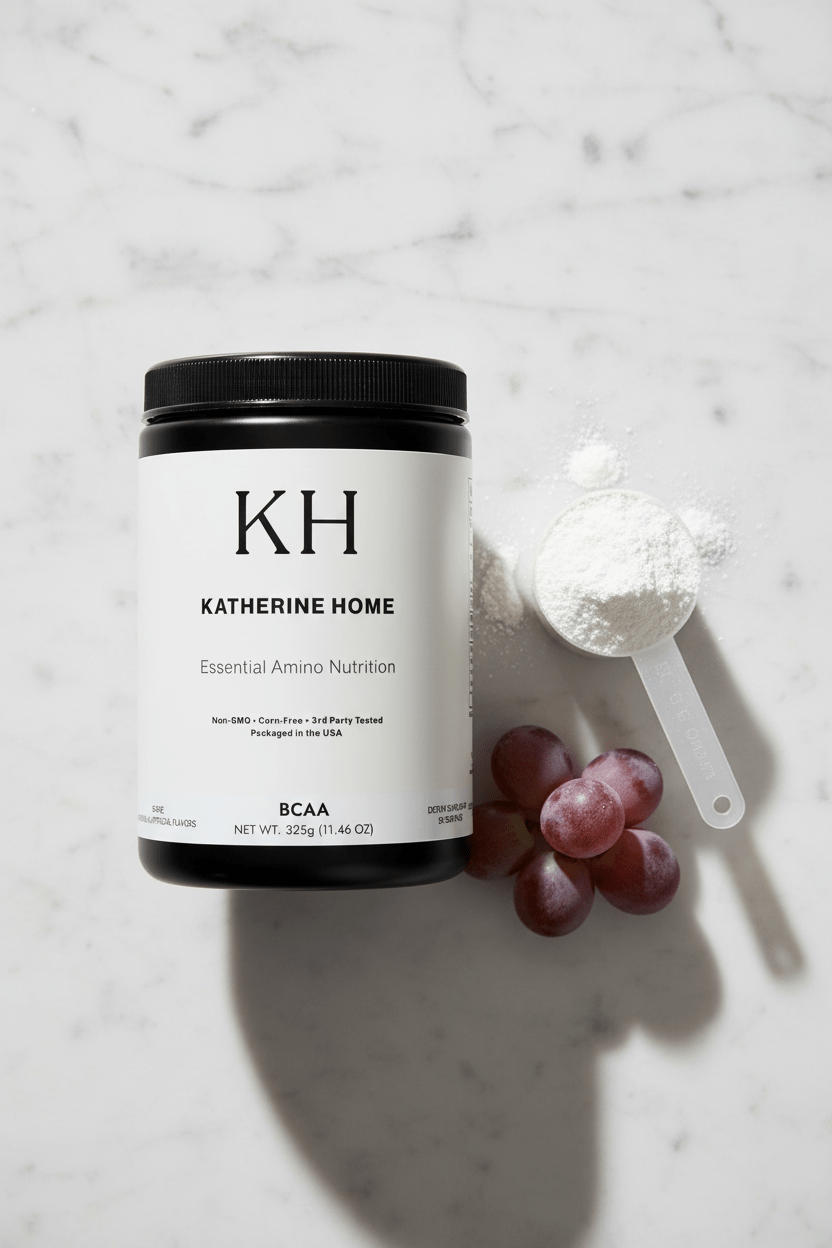 BCAA Supplement, Grape - KATHERINE HOMEFood SupplementsKATHERINE HOMEKATHERINE HOMETop view flat lay of Katherine Home BCAA Grape supplement with a white powder scoop and fresh grapes arranged on a neutral stone surface.