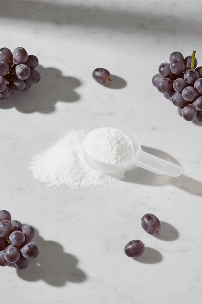 BCAA Supplement, Grape - KATHERINE HOMEFood SupplementsKATHERINE HOMEKATHERINE HOMEWhite scoop filled with fine BCAA powder beside the Katherine Home BCAA Grape supplement, accented with fresh grapes on a light stone surface.