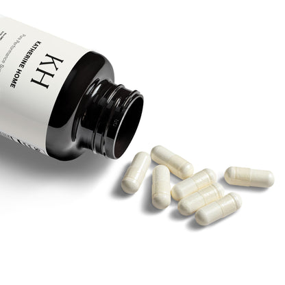 Open Katherine Home L-Arginine Supplement bottle with capsules spilling out on white background.