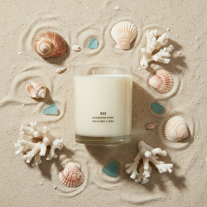 Ocean Mist & Moss Scented Candle surrounded by seashells and coral on sand, capturing coastal freshness and serenity.