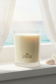 Ocean Mist & Moss Scented Candle on windowsill with ocean view, evoking coastal freshness and tranquility.