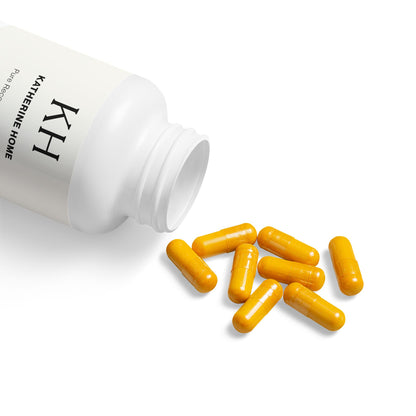 Open bottle of Katherine Home Turmeric with BioPerine Supplement showing bright yellow capsules spilling out.